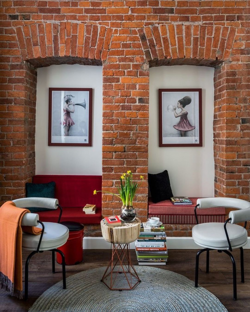 гостиная с кирпичными стенами, ярко-красным диванчиком, журнальным столиком из сруба на металлическом каркасе и белыми круглыми стульями.jpg