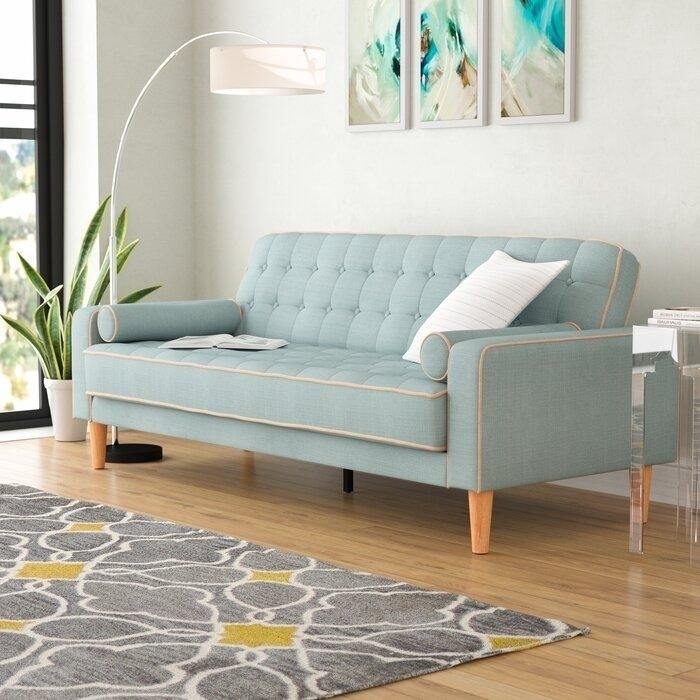 светлая гостиная со светло-бирюзовым диваном с валиками , серым ковром с горчичными акцентами, белым изогнутым торшером и триптихом над диваном.jpeg