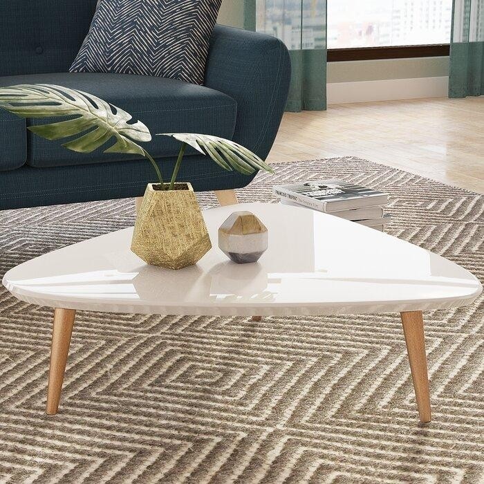 треугольный лакированный столик на деревянных конических ножках в гостиной с изумрудным диваном.jpeg