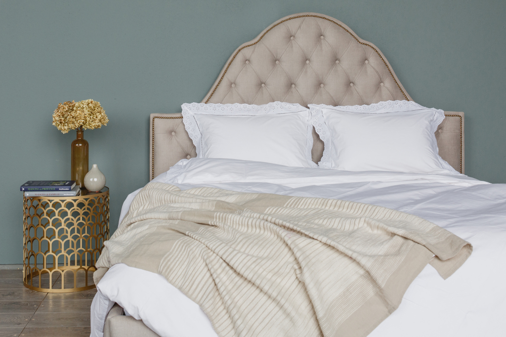 спальня со светлой кроватью с фигурным изголовьем и золотым журнальным столиком в качестве прикроватной тумбочки